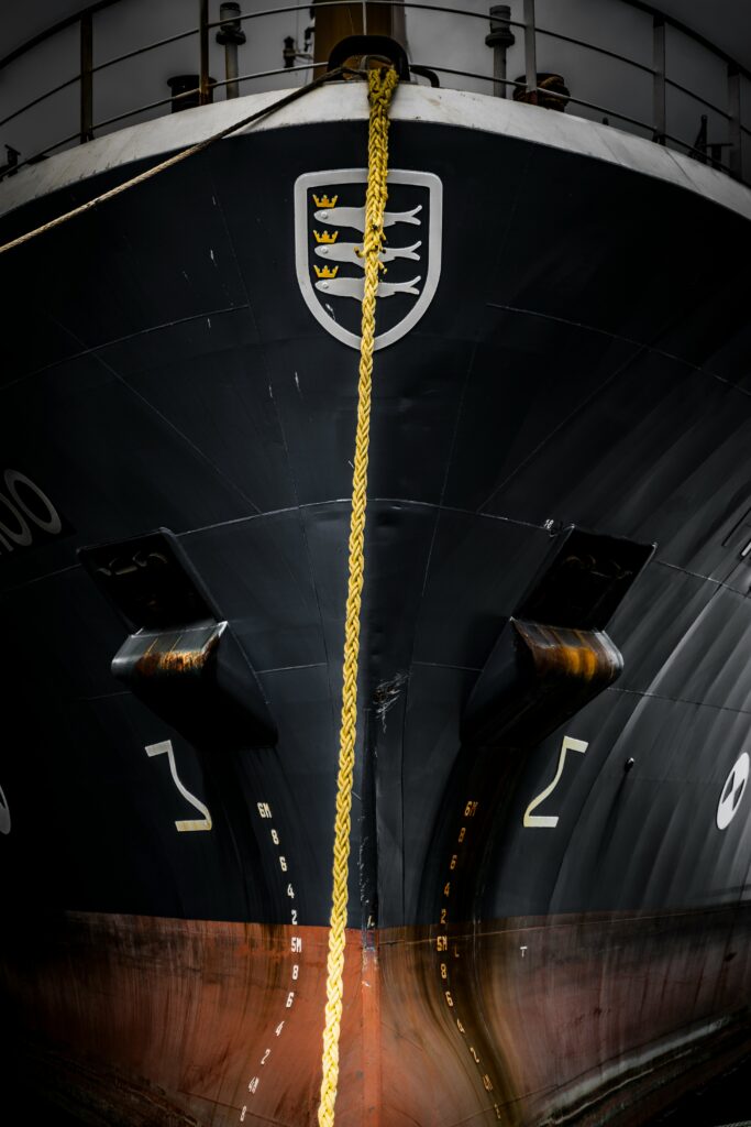 Baug på maritimt fartøy ved kai med fortøyningstau og skipsmerke, brukt i sammenheng med maritime installasjoner og tekniske miljøer.